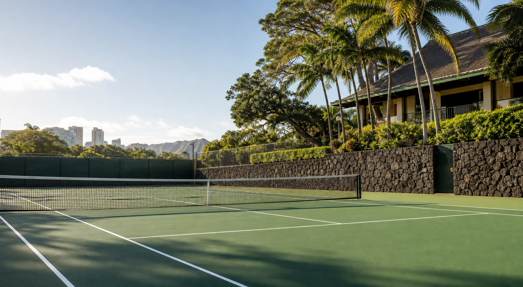 Historic Honolulu tennis court with lava rock wall and tropical foliage