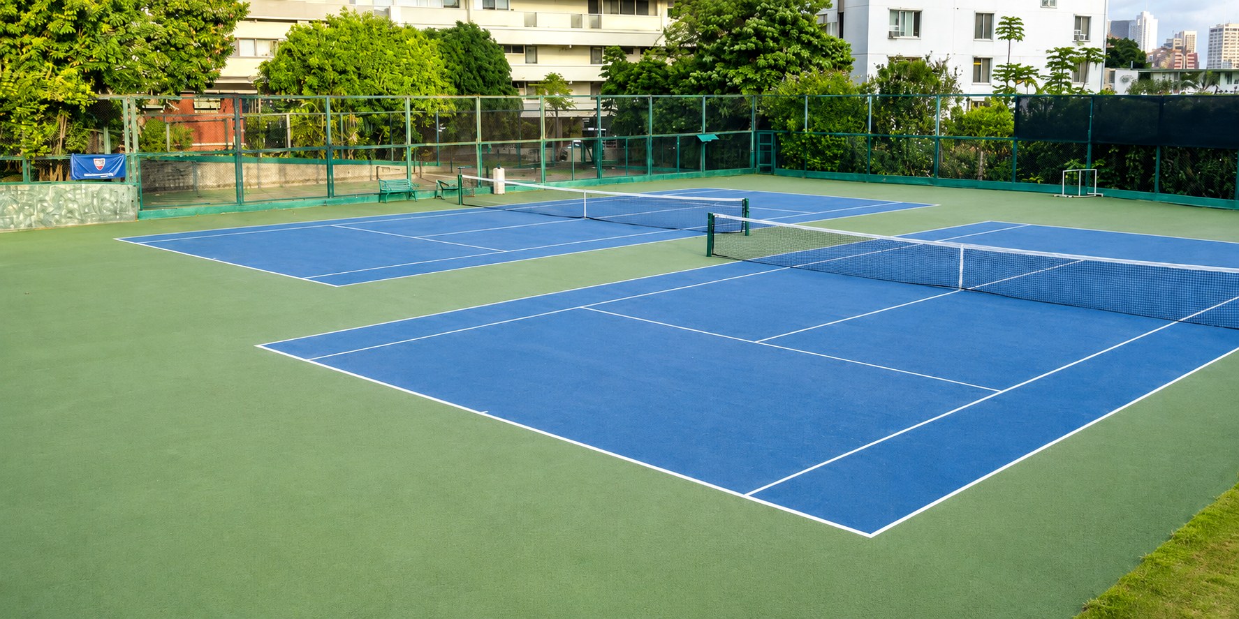 The two blue hard courts at Beretania Tennis Club, framed by tropical greenery and Honolulu high-rises